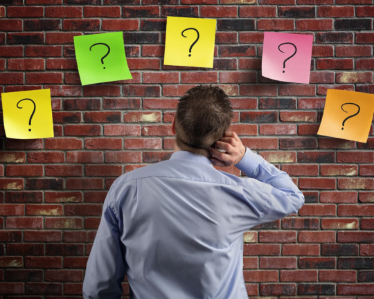 man staring at bring wall with posters of questions marks, confused
